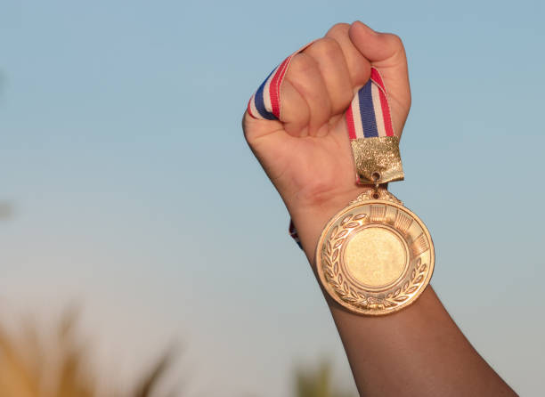 istock hand raised and holding gold medal against sky. award concept 938005156