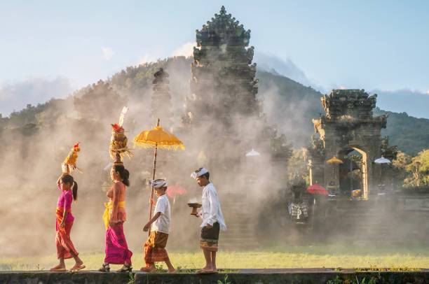 バリ島のヒンズー教の寺院 (pura) に母と子の散歩として伝統的なバリの男性と女性の儀式服と宗教的な製品を示します。 - indonesian ethnicity ストックフォトと画像