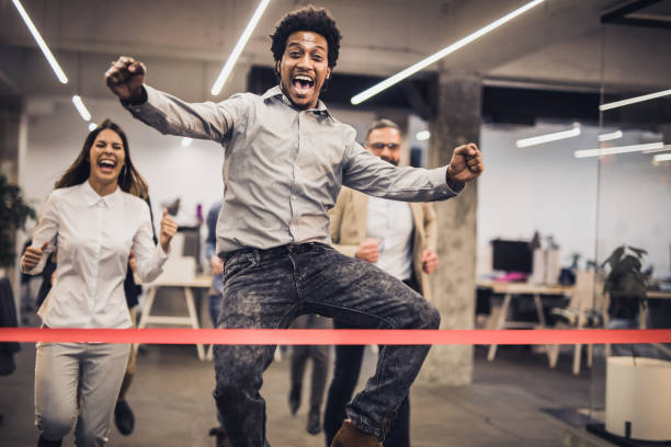 Cheerful African American freelancer celebrating the victory in sports race at casual office. Joyful black entrepreneur having fun while celebrating winning in race at casual office and looking at camera. race office stock pictures, royalty-free photos & images