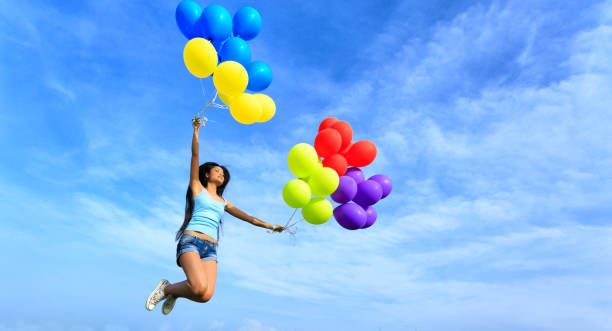 istock Cheerful young woman holding multicolored balloons jumping 938031540