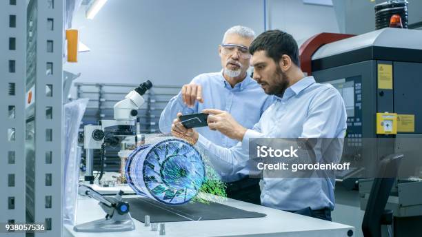 Two Engineers Works With Mobile Phone Using Augmented Reality Holographic Projection 3d Model Of The Engine Turbine Prototype Development Of Virtual Mixed Reality Application Stock Photo - Download Image Now