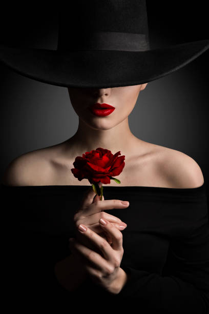 frau mit hut, die rose blume in händen, fashion model beauty portrait, rote lippen und schwarz breite krempe hut - beautiful image head and shoulders vertical stock-fotos und bilder