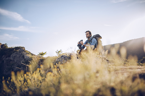 Young handsome hiker watching landscape and holding binoculars on the top of a mountain