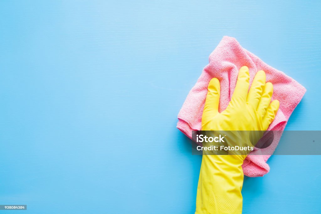 Employee hand in rubber protective glove with microfiber rag wiping blue table, wall or floor surface in room, bathroom, kitchen. Early spring or regular cleanup. Commercial cleaning company concept. Cleaning Stock Photo