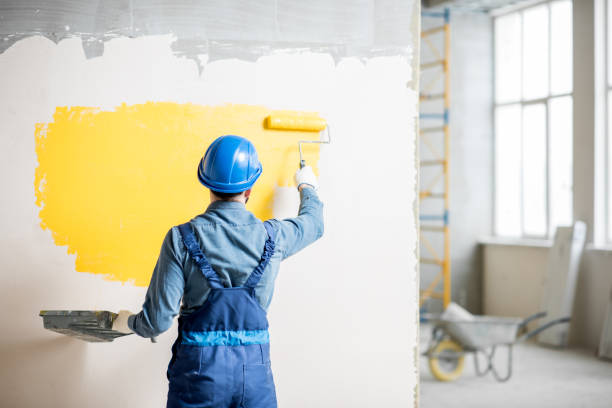Workamn painting wall indoors Workman in uniform painting wall with yellow paint at the construction site indoors paintings stock pictures, royalty-free photos & images