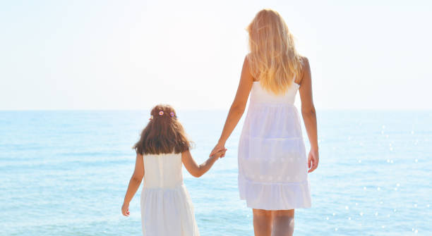 istock Mother and daughter standing on beach and watching sunset 938091606