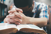istock Man praying, hands clasped together on her Bible. 938108512