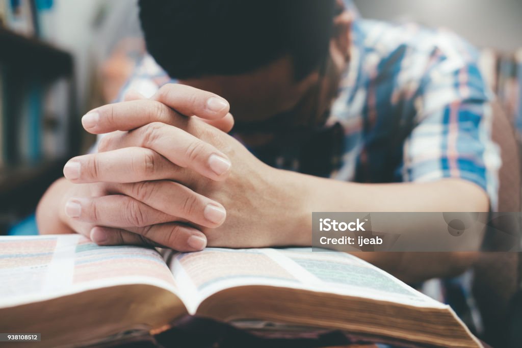 Man praying, hands clasped together on her Bible. Religion, Christianity, Praying.  Man praying, hands clasped together on her Bible. Praying Stock Photo