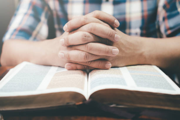 istock Man praying, hands clasped together on her Bible. 938108520