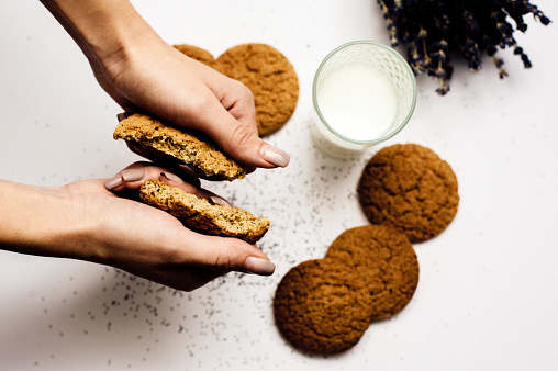 High angle view of milk and female hands breaking a cookie in half.