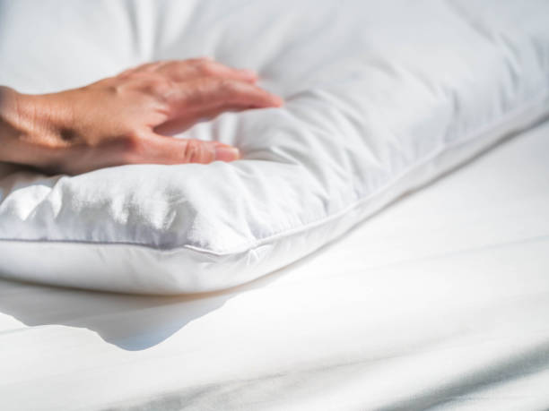 Close-up of white pillowcase on the bed with bedding cover in the bedroom and woman 's hand. stock photo