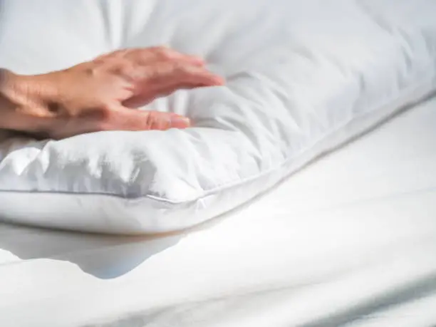 Close-up of white pillowcase on the bed with bedding cover in the bedroom and woman 's hand.