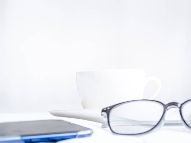 istock White coffee cup, eyeglasses, mobile phone with the white floor and gray wall. 938128664