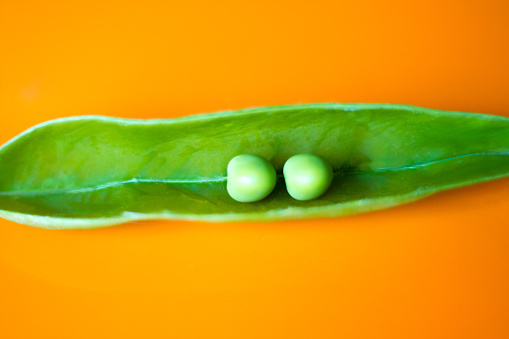 Two perfect peas in a pod on a vibrant orange background with plenty of copy space available.