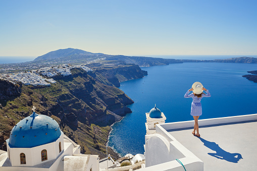 Young woman stands on a hill and looks at the marine landscape of Santorini, Greece