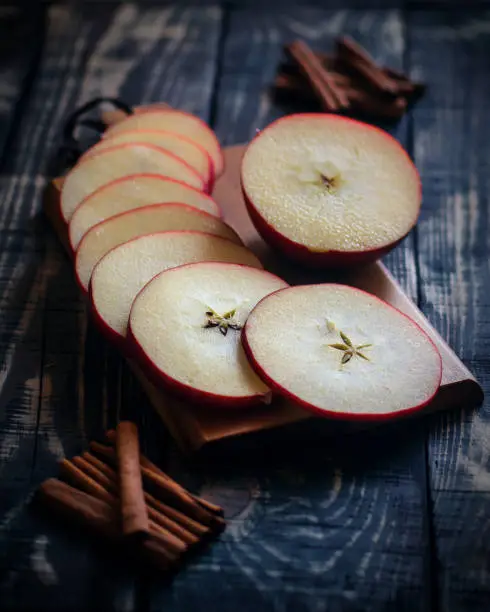 Sliced Red apples and brown cinnamon sticks on a wooden background symbolize Christmas and New Year