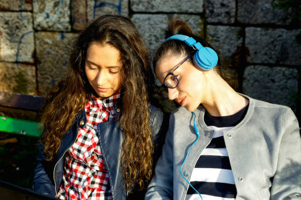istock Female friends sitting on bench in park talking using laptop in park 938148572