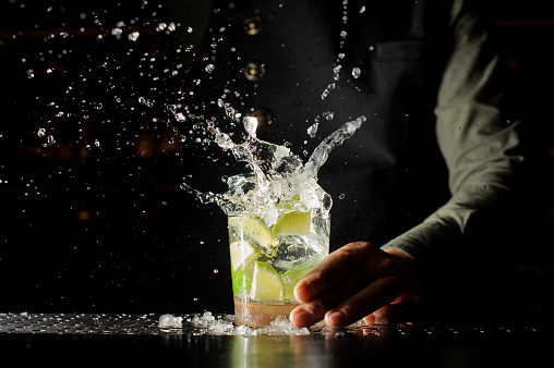 Cocktail splash with ice cubes and lime. Preparing of the delicious fresh cocktail on the bar stand