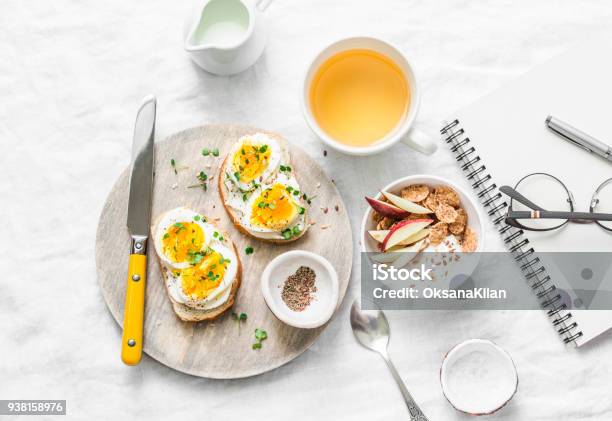 Photo libre de droit de Matin Petit Déjeuner Table Source Dinspiration Sandwiches Au Fromage À La Crème Et Le Œuf À La Coque Yogourt Aux Pommes Et Graines De Lin À Base De Plantes Detox Thé Portable Lunettes Sur Fond Clair Vue De Dessus Poser De Plat banque d'images et plus d'images libres de droit de Petit déjeuner