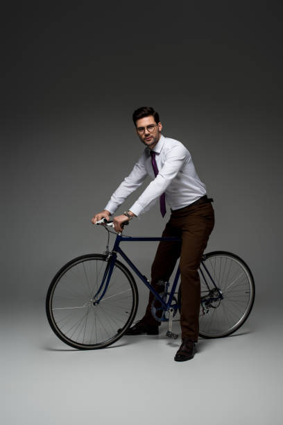 stylish businessman in glasses sitting on bicycle on grey