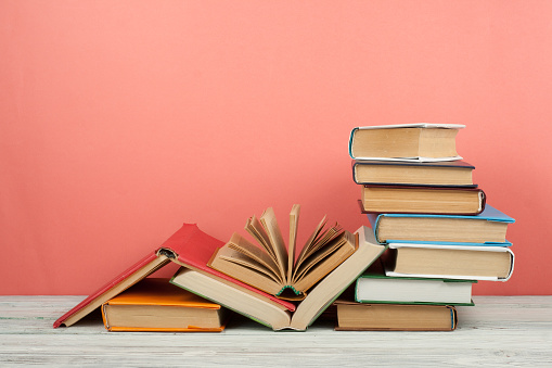 Book stacking. Open book, hardback books on wooden table and pink background. Back to school. Copy space for text.