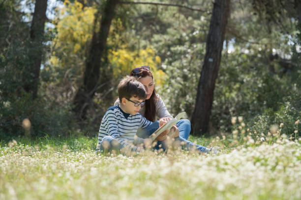 istock Beautiful women and her son sitting in forest and reading book 938174574