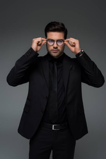 istock Man in stylish black suit taking off glasses isolated on grey 938175486