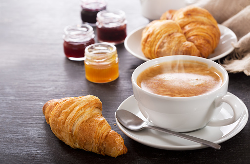 breakfast with cup of coffee and croissants on dark table