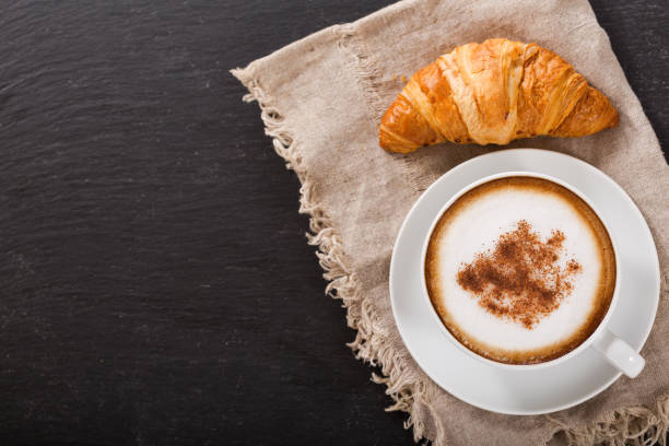 istock Cup of cappuccino coffee and croissant on dark table 938175600