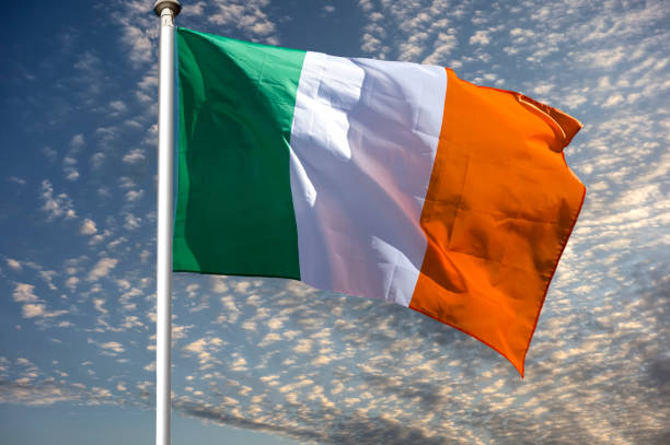 istock Irish flag over blue sky with white clouds 938177972