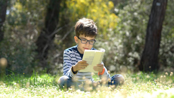 criança feliz, lendo um livro na floresta - child glasses elementary student reading - fotografias e filmes do acervo