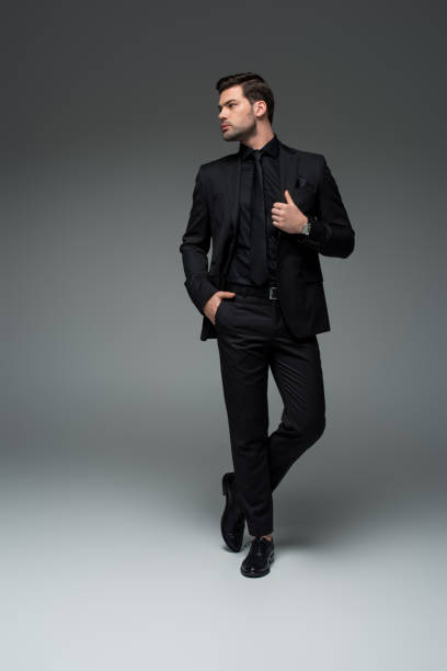 istock Young stylish man in black suit posing on grey 938179234