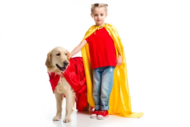 Dog in red cape with supergirl in yellow cape standing beside isolated on white