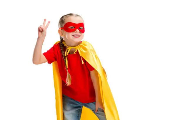 Smiling supergirl in yellow cape and red mask for eyes gesturing peace sign isolated on white