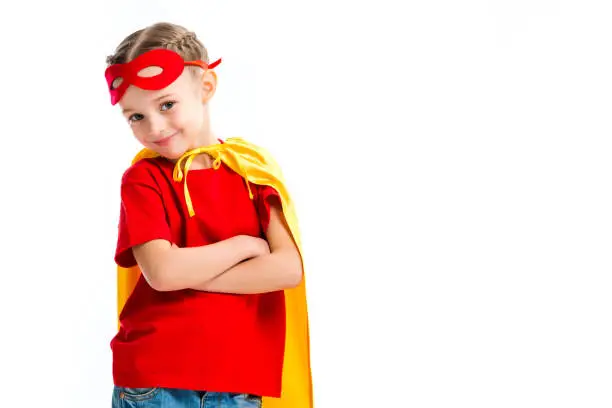 Smiling little supergirl wearing yellow cape with red mask for eyes on forehead isolated on white