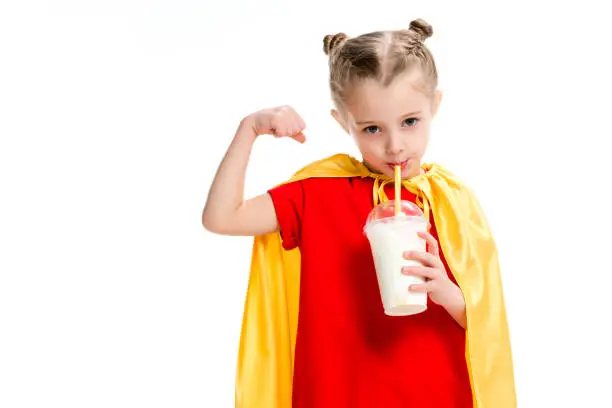 Little supergirl drinking milkshake and showing muscles isolated on white