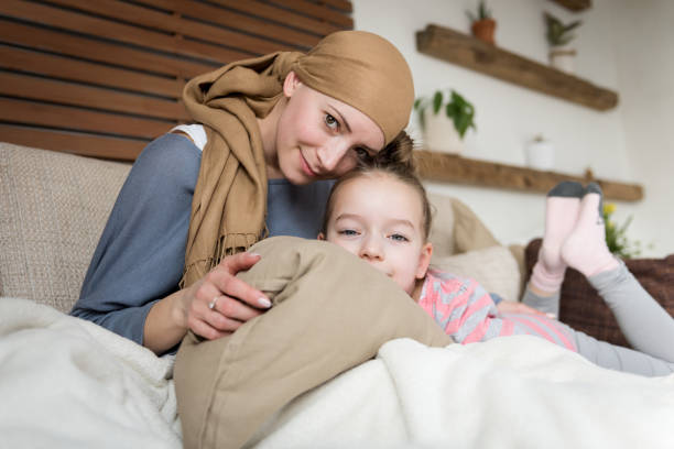 giovane paziente oncologico adulta che trascorre del tempo con sua figlia a casa, rilassandosi sul divano. concetto di cancro e sostegno familiare. - cancer chemotherapy drug baby family foto e immagini stock