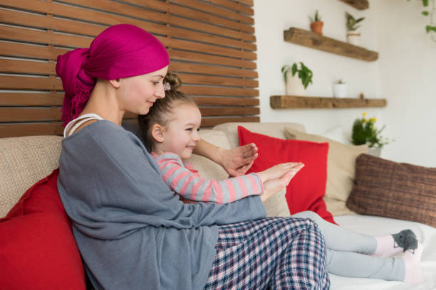 giovane paziente oncologico adulta che trascorre del tempo con sua figlia a casa, rilassandosi sul divano. concetto di cancro e sostegno familiare. - cancer chemotherapy drug baby family foto e immagini stock