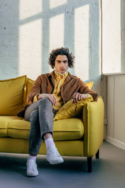 istock Young stylish man with eyeglasses in hand sitting on couch 938229934