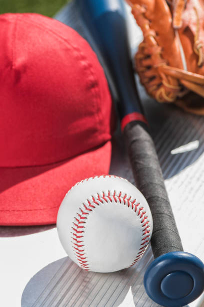 un primer plano de una pelota de béisbol nuevo, un gorro rojo, guante de béisbol y bate en banco - little league - baseball bat baseball little league baseballs fotografías e imágenes de stock