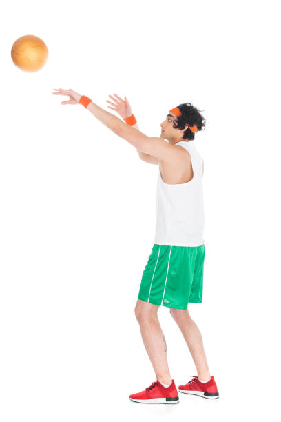 A wide portrait shot of a mature woman enjoying an outdoor netball session on a sports court during a cold, sunny day. The woman has thrown a red netball towards the hoop while concentrating as she is trying to score. They are dressed in warm sports clothing on a sunny winter's day in Northumberland, North East England.\n\nVideos are available similar to this scenario.