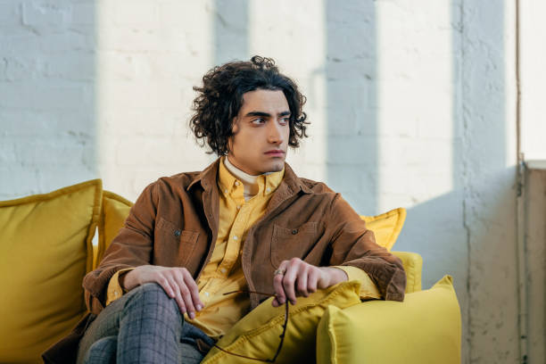 istock Young stylish man with eyeglasses in hand sitting on couch 938234648