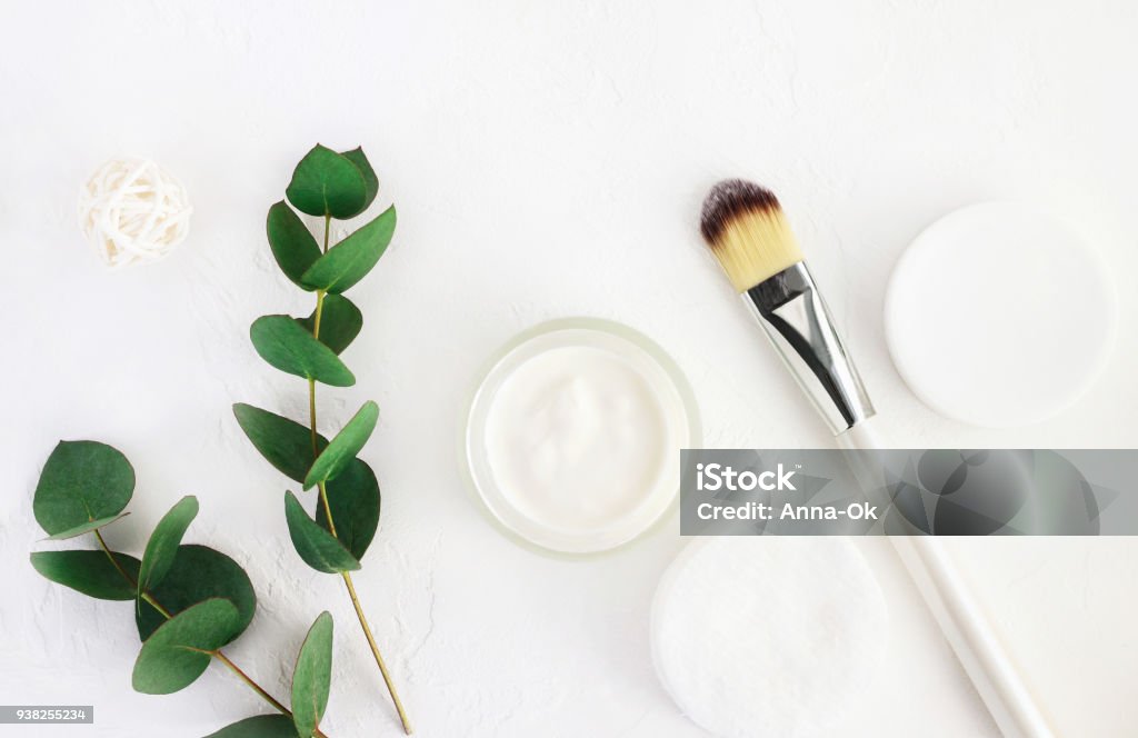 Skincare cosmetics with aroma eucalyptus plant extract. Home spa and body care. Jar of organic beauty product and application brush with fresh green leaves herbal bough, top view white background. Skin Care Stock Photo