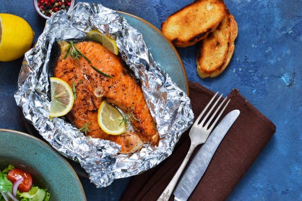 Baked in a foil steak salmon with a lemon and a marble on a wooden background. stock photo
