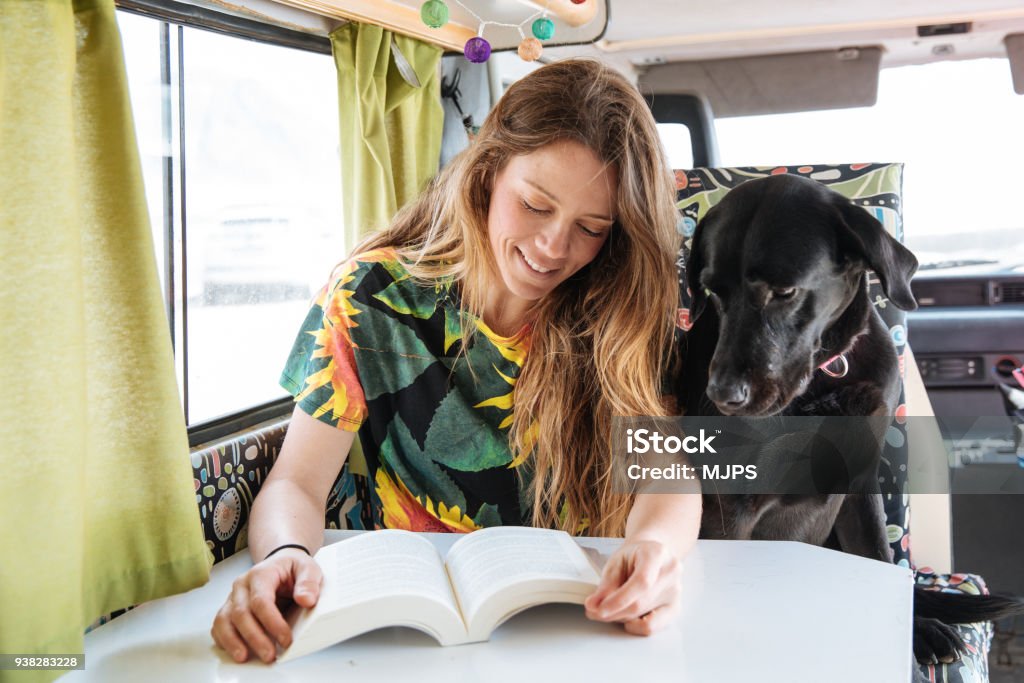 heureuse jeune femme lisant un livre dans son camping-car - Photo de Chien libre de droits