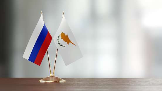 Cypriot and Russian flag pair on desk over defocused background. Horizontal composition with copy space and selective focus.