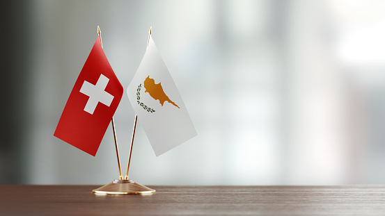 Cypriot and Swiss flag pair on desk over defocused background. Horizontal composition with copy space and selective focus.