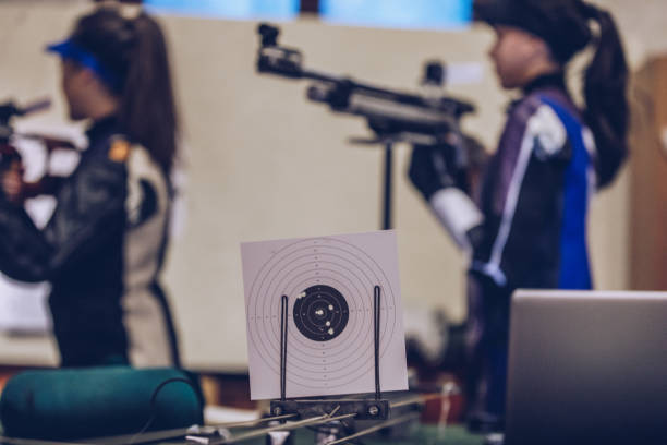 Two women, girls sport shooters aiming with a rifle on target shooting training, shooting target of paper.