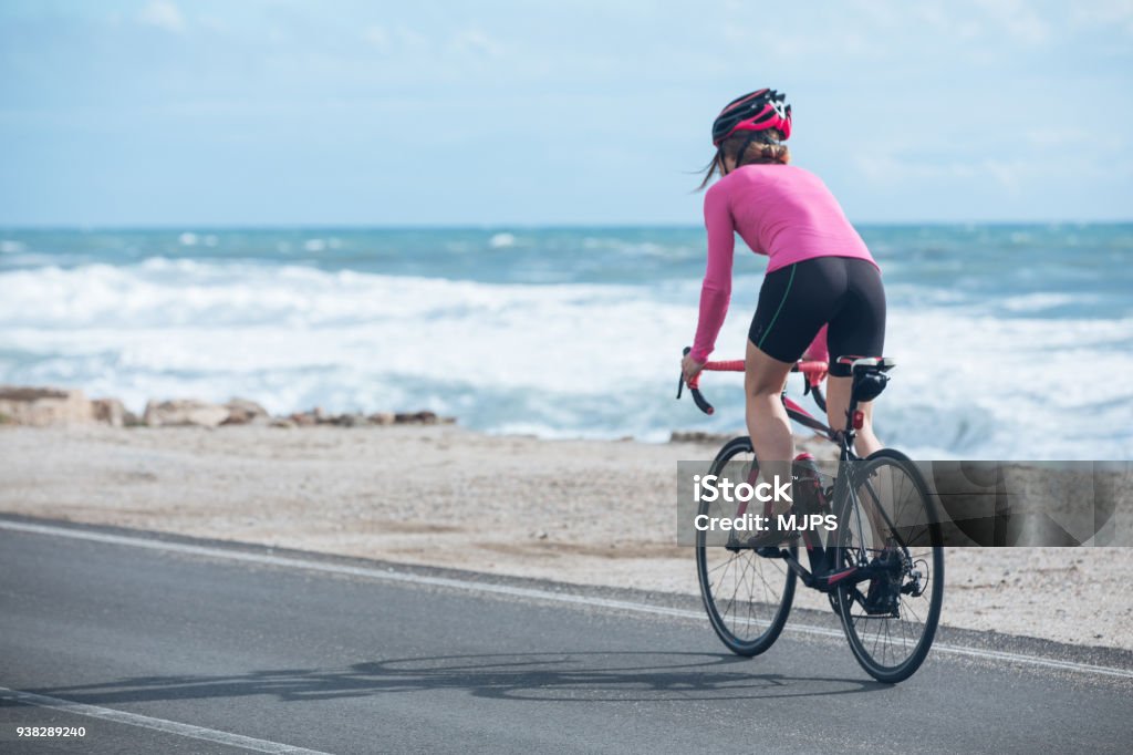ciclista mujer monta en bicicleta en la carretera cerca del mar - Foto de stock de Andar en bicicleta libre de derechos