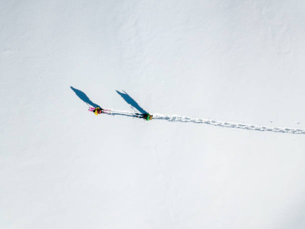 Two hikers with long shadows walking over snow (aerial shot)